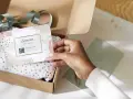 Tarjeta de agradecimiento tamaño postal con código QR, dentro de una caja abierta con papel de seda dorado.