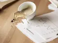 Café derramado sobre un gráfico de "Accounting period". El líquido, con un acabado glasofonado mate, salpica sobre el papel y la mesa de madera.