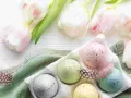 Huevos de Pascua en color pastel, salpicados y decorados con plumas, junto a tulipanes blancos y rosados.
