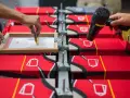 Manos aplicando tinta en un marco para serigrafía proceso sobre camisetas rojas. Otra mano usa secador.