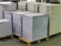 Grandes pilas de papel apiladas en palets, listas para ser impresas. Las medidas folio son evidentes en la cantidad de material.
