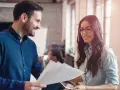 Hombre y mujer sonríen mientras revisan documentos, un ejemplo de cómo la publicidad social puede unir a las personas en el trabajo.