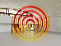 Círculos concéntricos rojos y amarillos que parecen flotar en un espacio arquitectónico moderno. Ejemplos de anamorfosis que transforman la percepción.