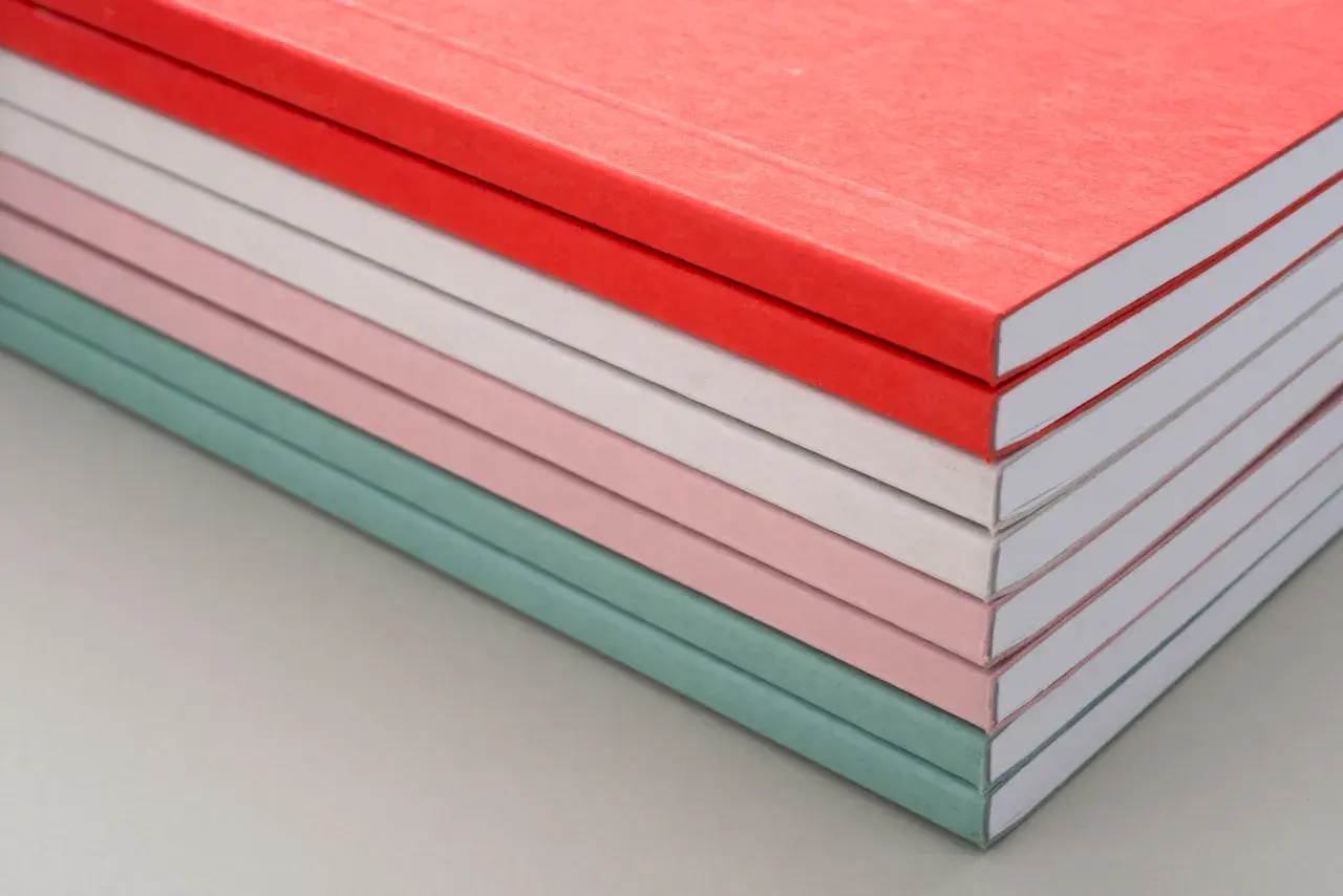 Una pila de cuadernos con diferentes tipos de encuadernación, en tonos pastel y rojo.