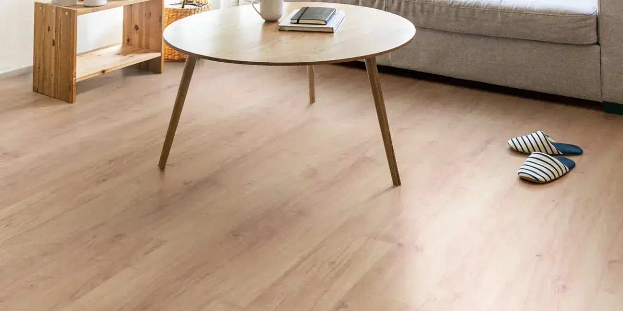 Un suelo de laminado vinilo claro y cálido ilumina un salón moderno con sofá gris, mesa de centro de madera y plantas.