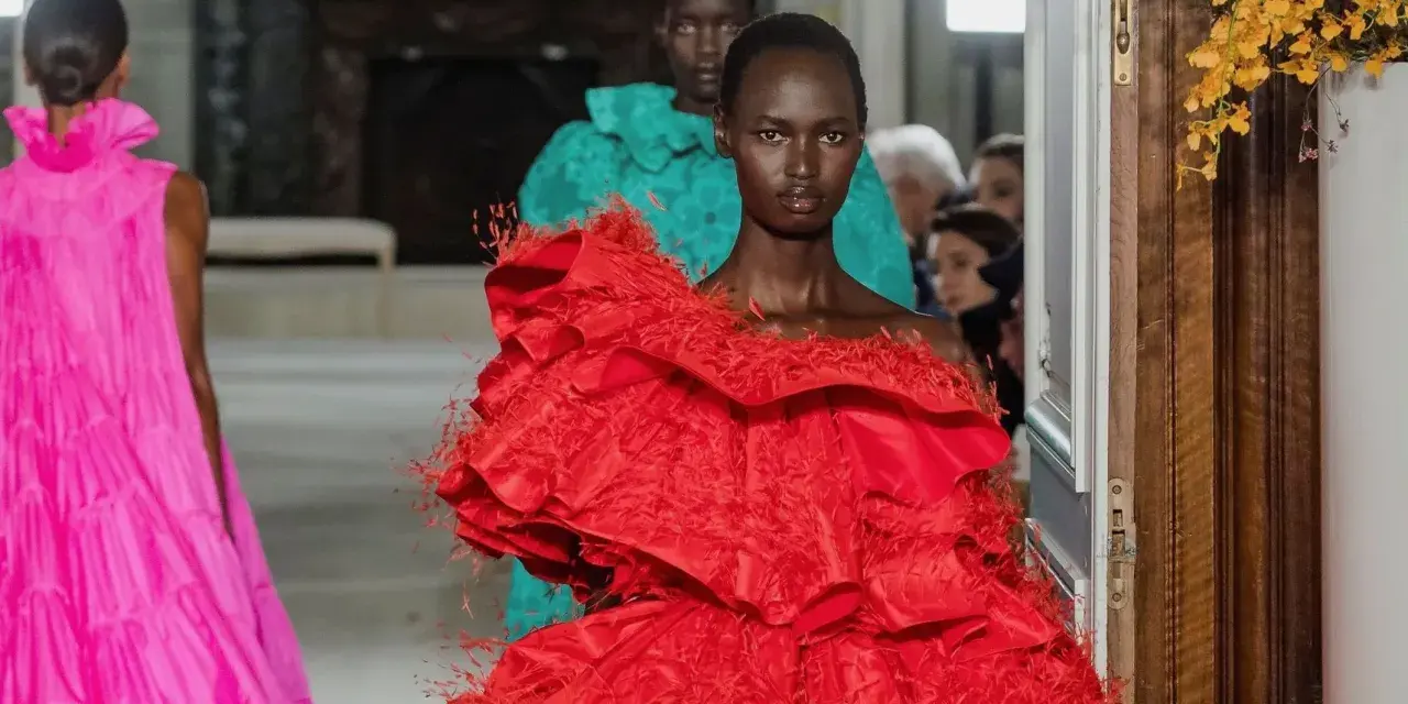 Una modelo luce un espectacular vestido rojo valentino con volantes y plumas. Detrás, otra modelo con un vestido turquesa.