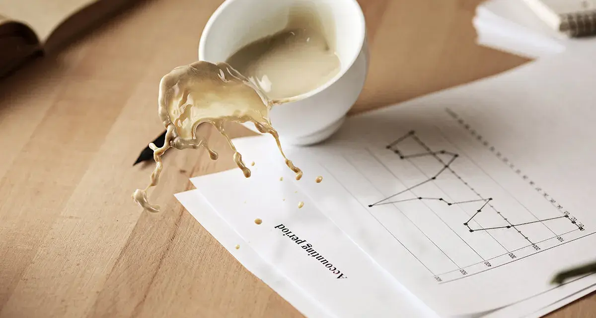 Café derramado sobre un gráfico de "Accounting period". El líquido, con un acabado glasofonado mate, salpica sobre el papel y la mesa de madera.