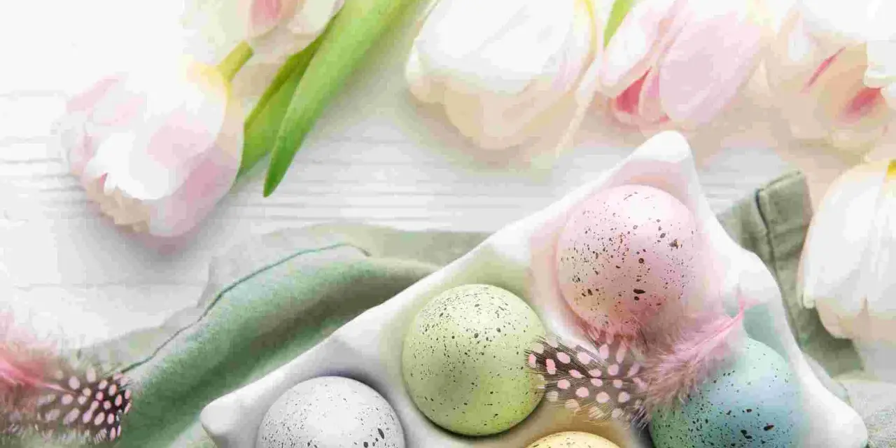 Huevos de Pascua en color pastel, salpicados y decorados con plumas, junto a tulipanes blancos y rosados.