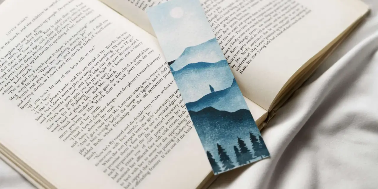 Un marcapáginas con un paisaje montañoso y árboles en acuarela, colocado sobre un libro abierto.