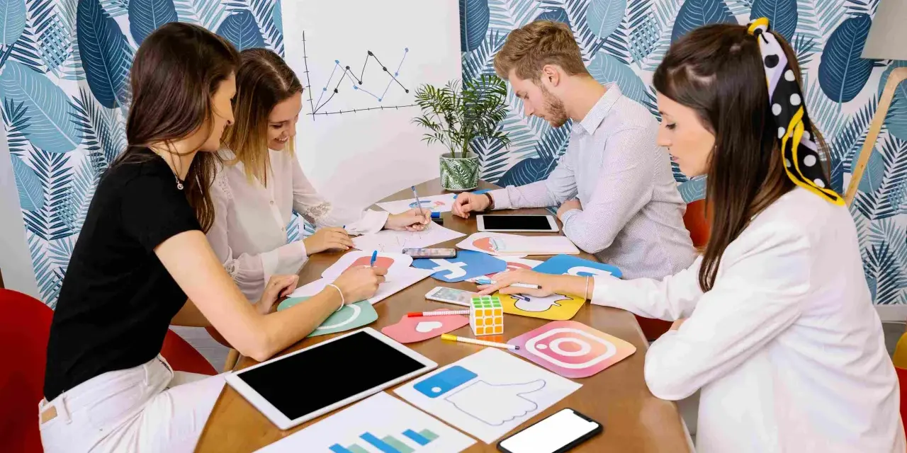 Equipo discutiendo estrategias de marketing digital, con iconos de redes sociales y gráficos. Parecen estar planeando una campaña de "fake out of home".
