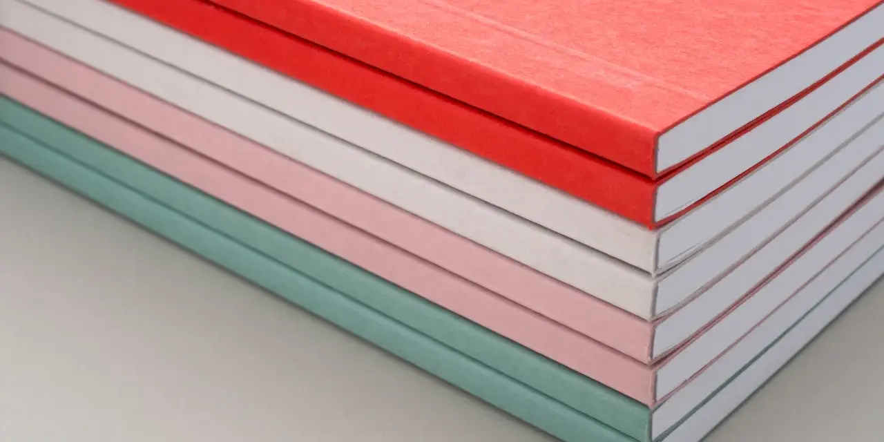 Una pila de cuadernos con diferentes tipos de encuadernación, en tonos pastel y rojo.