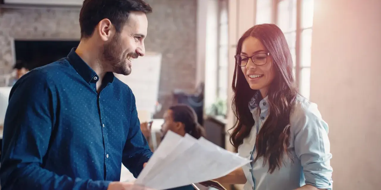 Hombre y mujer sonríen mientras revisan documentos, un ejemplo de cómo la publicidad social puede unir a las personas en el trabajo.