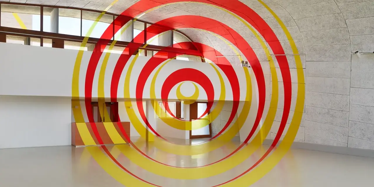 Círculos concéntricos rojos y amarillos que parecen flotar en un espacio arquitectónico moderno. Ejemplos de anamorfosis que transforman la percepción.