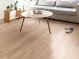 Un suelo de laminado vinilo claro y cálido ilumina un salón moderno con sofá gris, mesa de centro de madera y plantas.