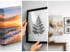 Un lienzo con un atardecer en la playa, una hoja de helecho enmarcada y arte abstracto sobre una mesa.