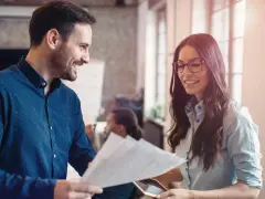 Hombre y mujer sonríen mientras revisan documentos, un ejemplo de cómo la publicidad social puede unir a las personas en el trabajo.