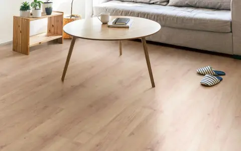 Un suelo de laminado vinilo claro y cálido ilumina un salón moderno con sofá gris, mesa de centro de madera y plantas.