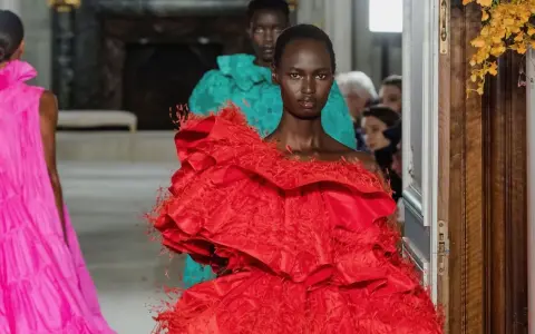 Una modelo luce un espectacular vestido rojo valentino con volantes y plumas. Detrás, otra modelo con un vestido turquesa.