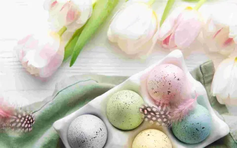 Huevos de Pascua en color pastel, salpicados y decorados con plumas, junto a tulipanes blancos y rosados.