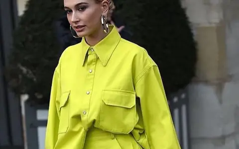 Modelo luce una camisa de **color lima** vibrante, con bolsillos frontales y grandes aros plateados.