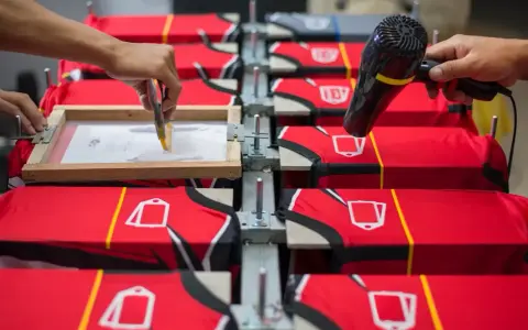 Manos aplicando tinta en un marco para serigrafía proceso sobre camisetas rojas. Otra mano usa secador.