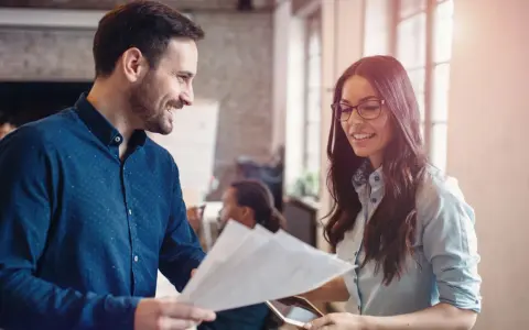Hombre y mujer sonríen mientras revisan documentos, un ejemplo de cómo la publicidad social puede unir a las personas en el trabajo.