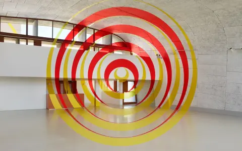 Círculos concéntricos rojos y amarillos que parecen flotar en un espacio arquitectónico moderno. Ejemplos de anamorfosis que transforman la percepción.