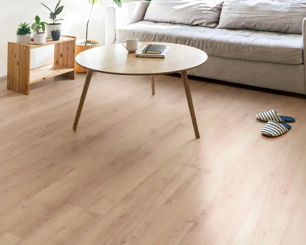 Un suelo de laminado vinilo claro y cálido ilumina un salón moderno con sofá gris, mesa de centro de madera y plantas.