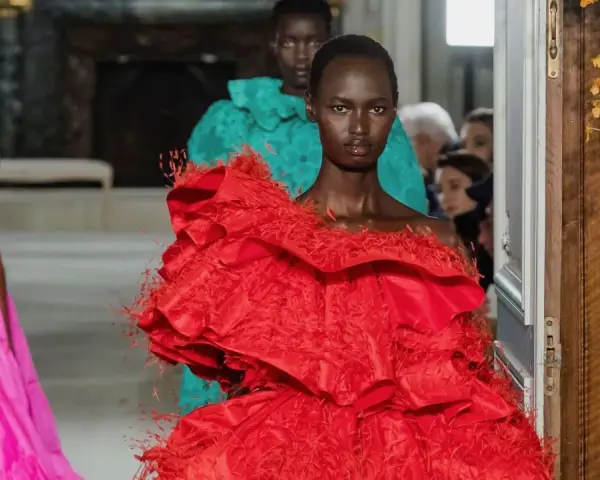 Una modelo luce un espectacular vestido rojo valentino con volantes y plumas. Detrás, otra modelo con un vestido turquesa.