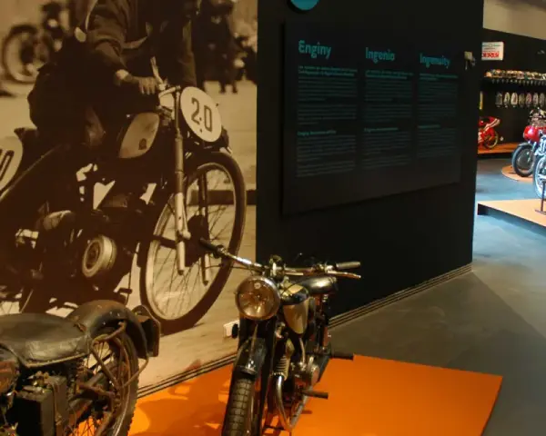 Exhibición de motocicletas clásicas con cartelas informativas. Destacan una Royal Enfield y una moto de competición con el número 31.