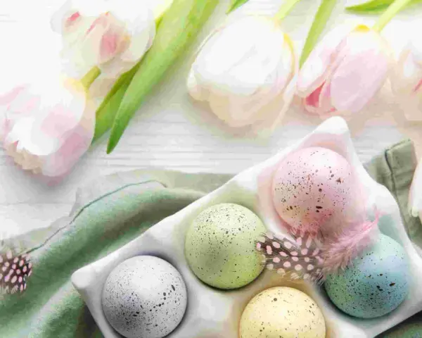 Huevos de Pascua en color pastel, salpicados y decorados con plumas, junto a tulipanes blancos y rosados.