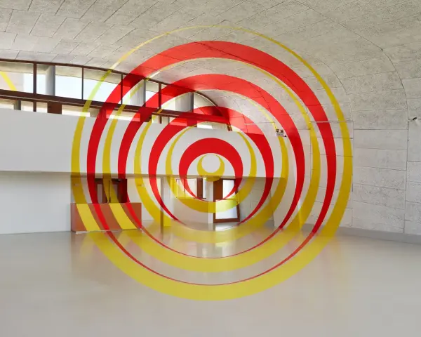 Círculos concéntricos rojos y amarillos que parecen flotar en un espacio arquitectónico moderno. Ejemplos de anamorfosis que transforman la percepción.