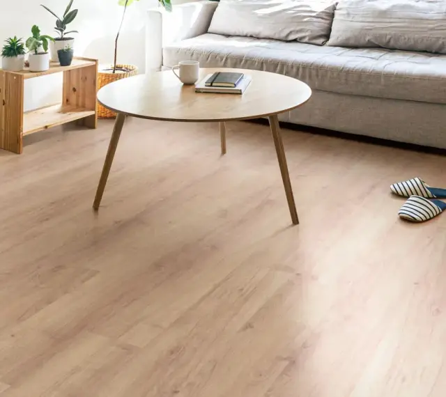 Un suelo de laminado vinilo claro y cálido ilumina un salón moderno con sofá gris, mesa de centro de madera y plantas.