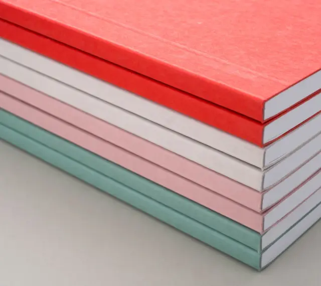 Una pila de cuadernos con diferentes tipos de encuadernación, en tonos pastel y rojo.