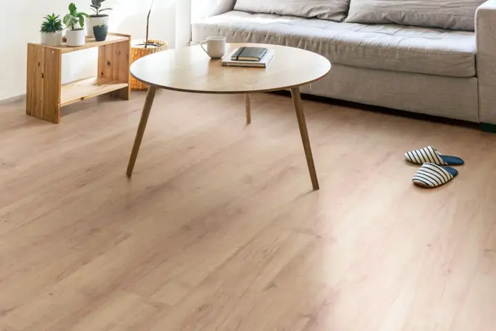 Un suelo de laminado vinilo claro y cálido ilumina un salón moderno con sofá gris, mesa de centro de madera y plantas.
