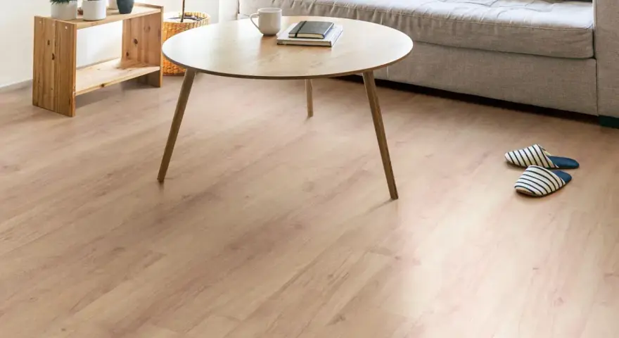 Un suelo de laminado vinilo claro y cálido ilumina un salón moderno con sofá gris, mesa de centro de madera y plantas.