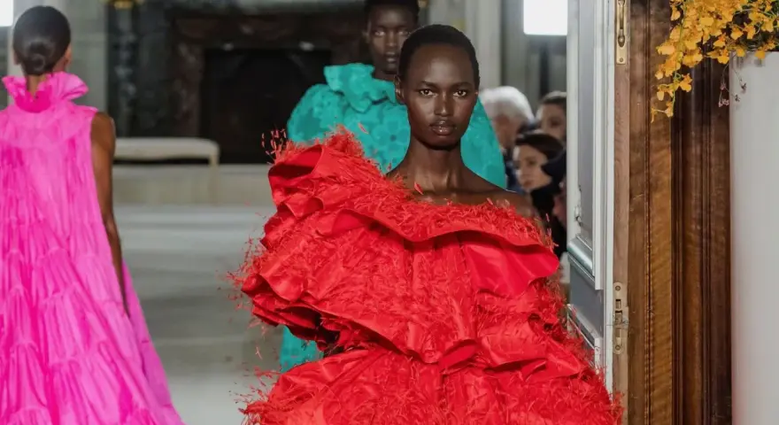 Una modelo luce un espectacular vestido rojo valentino con volantes y plumas. Detrás, otra modelo con un vestido turquesa.