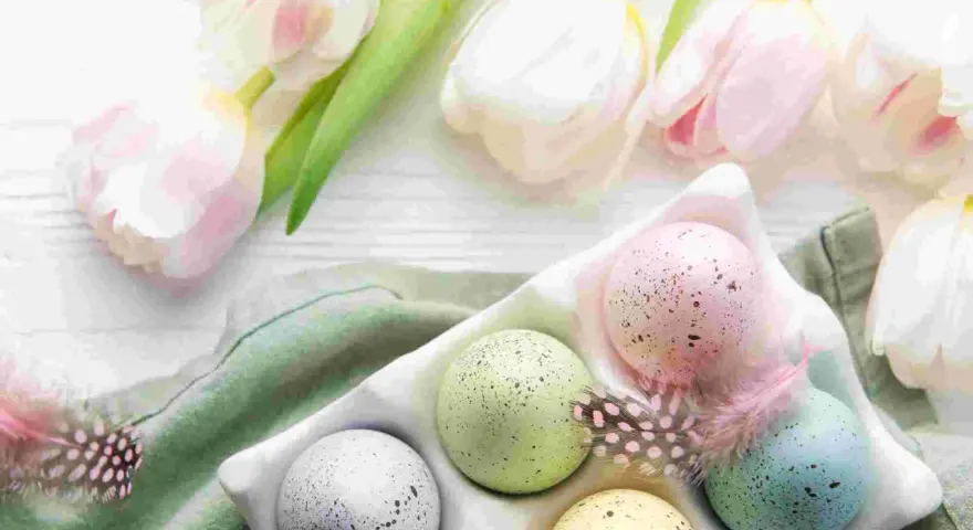 Huevos de Pascua en color pastel, salpicados y decorados con plumas, junto a tulipanes blancos y rosados.