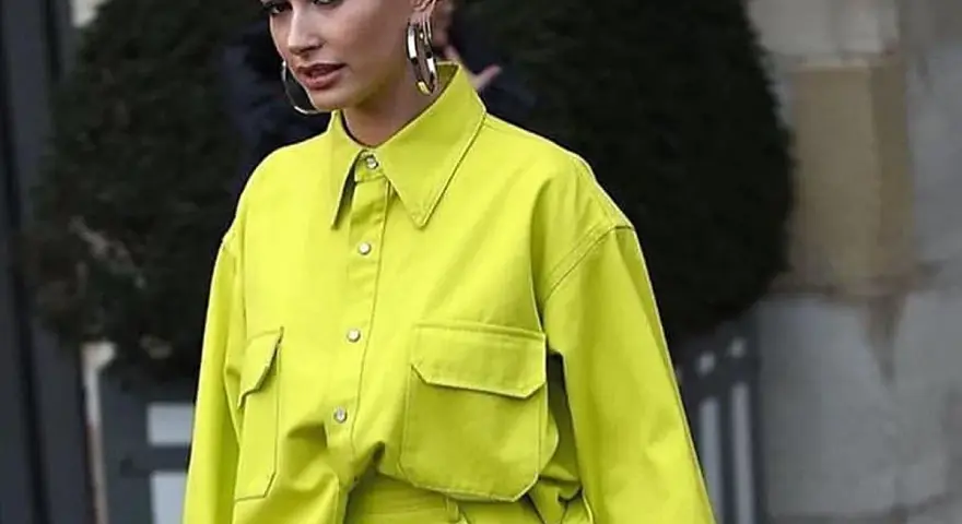 Modelo luce una camisa de **color lima** vibrante, con bolsillos frontales y grandes aros plateados.