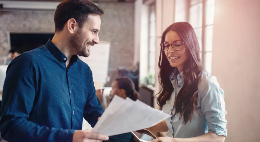 Hombre y mujer sonríen mientras revisan documentos, un ejemplo de cómo la publicidad social puede unir a las personas en el trabajo.