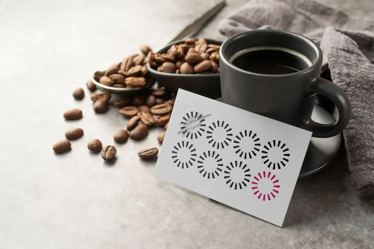 Una taza de café junto a granos y una tarjeta de fidelización con círculos que se van completando.