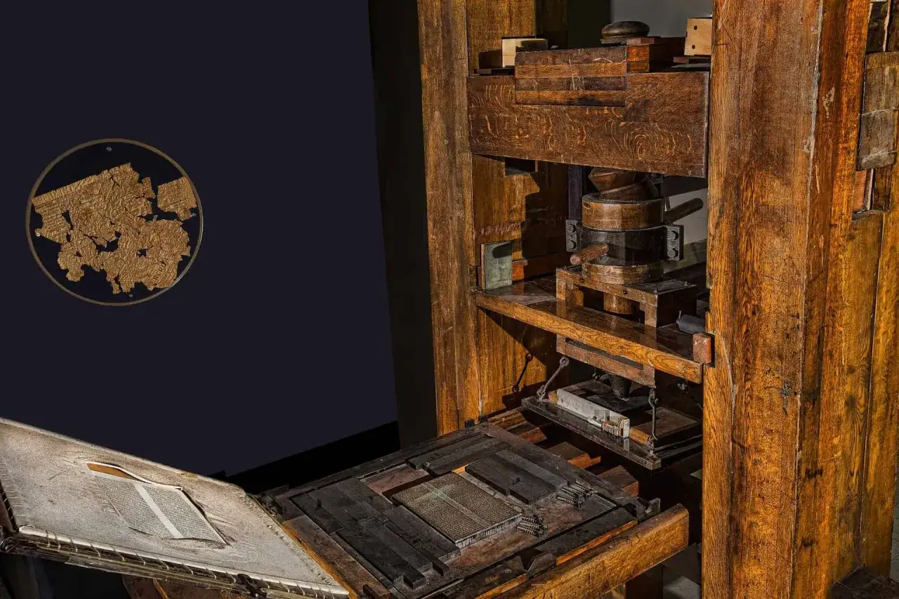M&aacute;quina de imprenta antigua de madera, similar a la que us&oacute; quien invent&oacute; la imprenta. Detalle de tipos m&oacute;viles y un libro abierto.