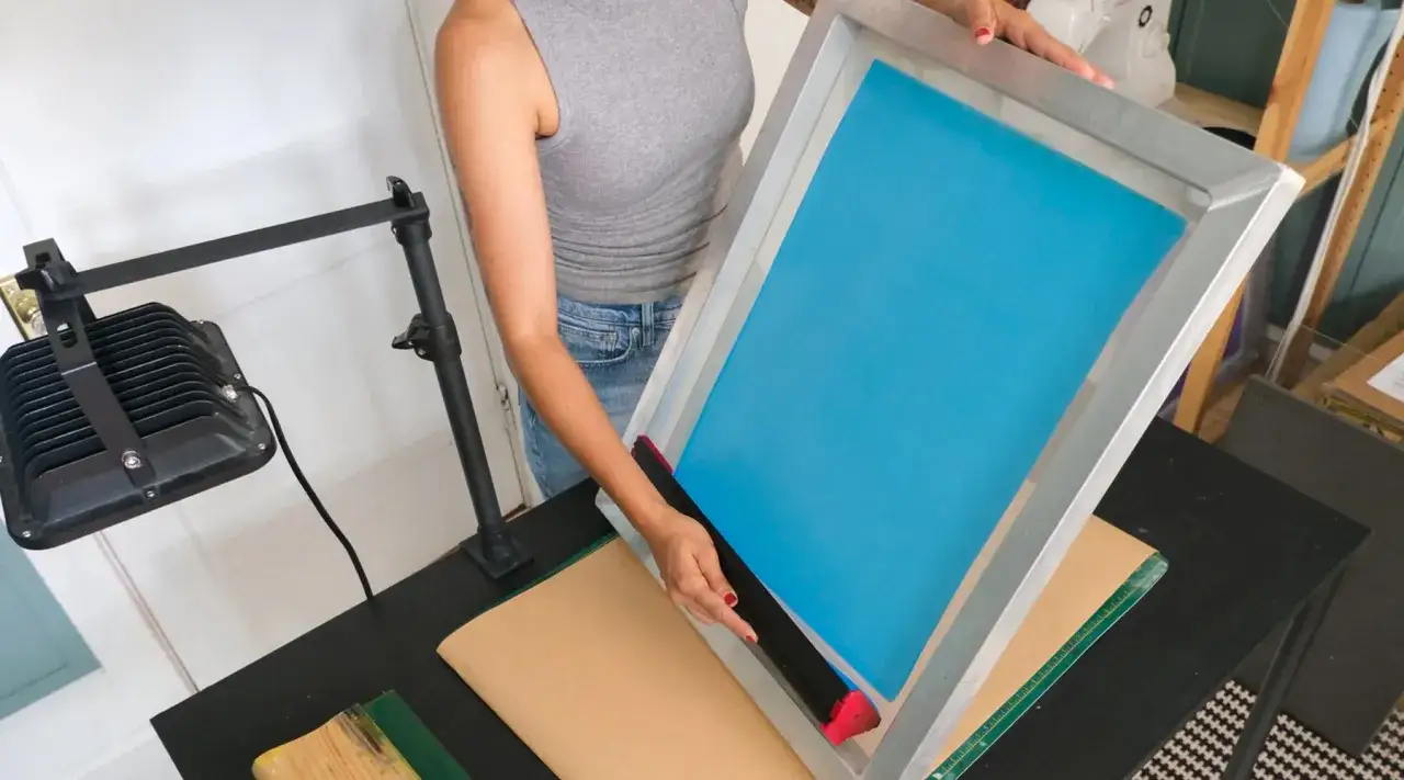 Persona prepara un marco de serigraf&iacute;a con una rasqueta para el proceso de impresi&oacute;n.
