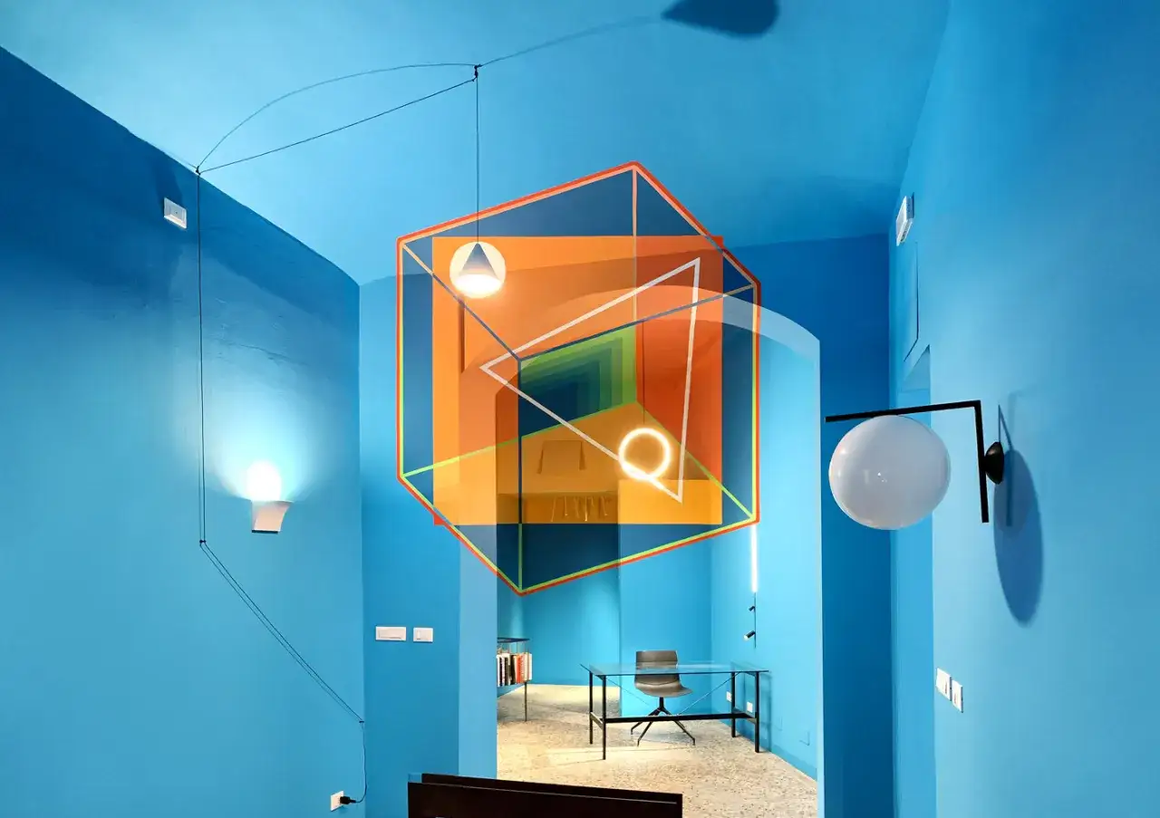 Un cubo naranja con l&iacute;neas blancas y un t&uacute;nel de perspectiva, como ejemplos de anamorfosis, flota en una habitaci&oacute;n azul brillante con l&aacute;mparas modernas.
