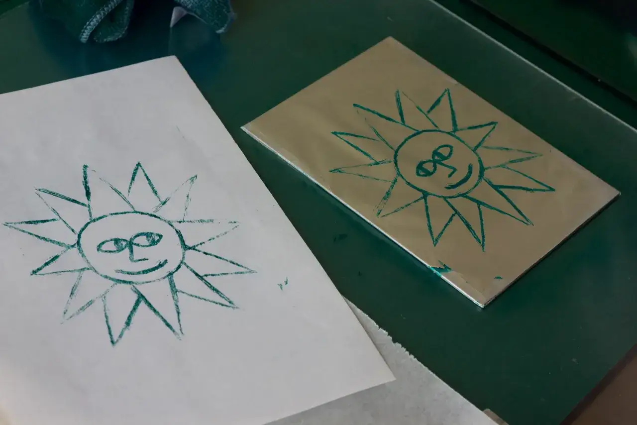 Dos soles sonrientes, uno en papel y otro en una placa met&aacute;lica, como parte de una litograf&iacute;a casera.