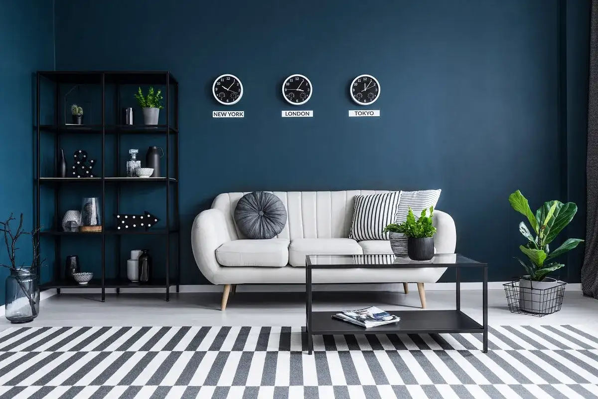 Sof&aacute; blanco y estanter&iacute;a negra sobre pared color azul marino. Tres relojes marcan la hora de Nueva York, Londres y Tokio.
