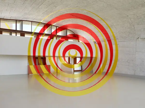 Círculos concéntricos rojos y amarillos que parecen flotar en un espacio arquitectónico moderno. Ejemplos de anamorfosis que transforman la percepción.
