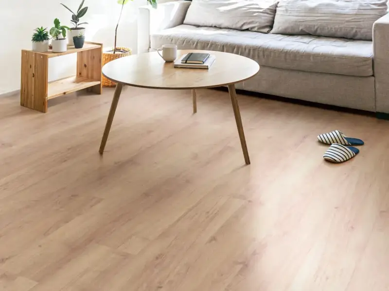 Un suelo de laminado vinilo claro y cálido ilumina un salón moderno con sofá gris, mesa de centro de madera y plantas.