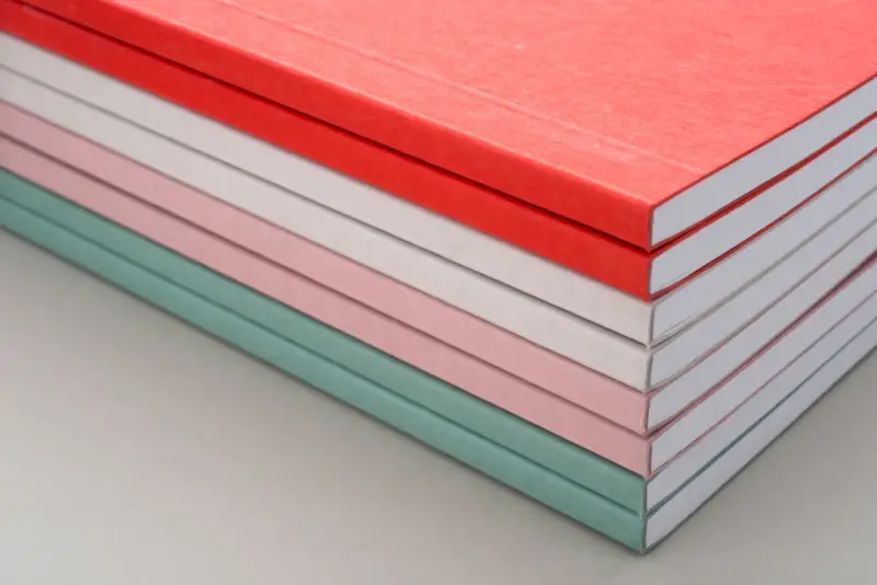 Una pila de cuadernos con diferentes tipos de encuadernación, en tonos pastel y rojo.
